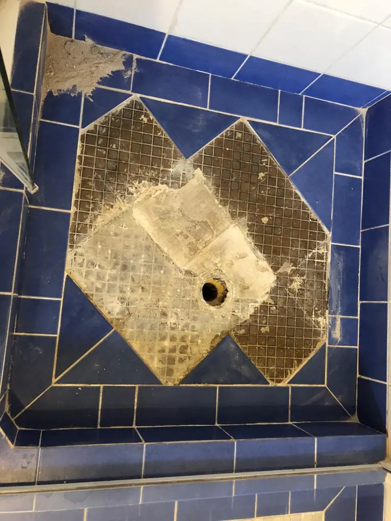 Before: Blue-tiled shower base with the centre floor tiles removed around the waste