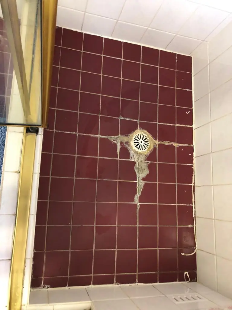 Before: Burgundy-tiled shower floor with a cracked, patched area running from the floor waste
