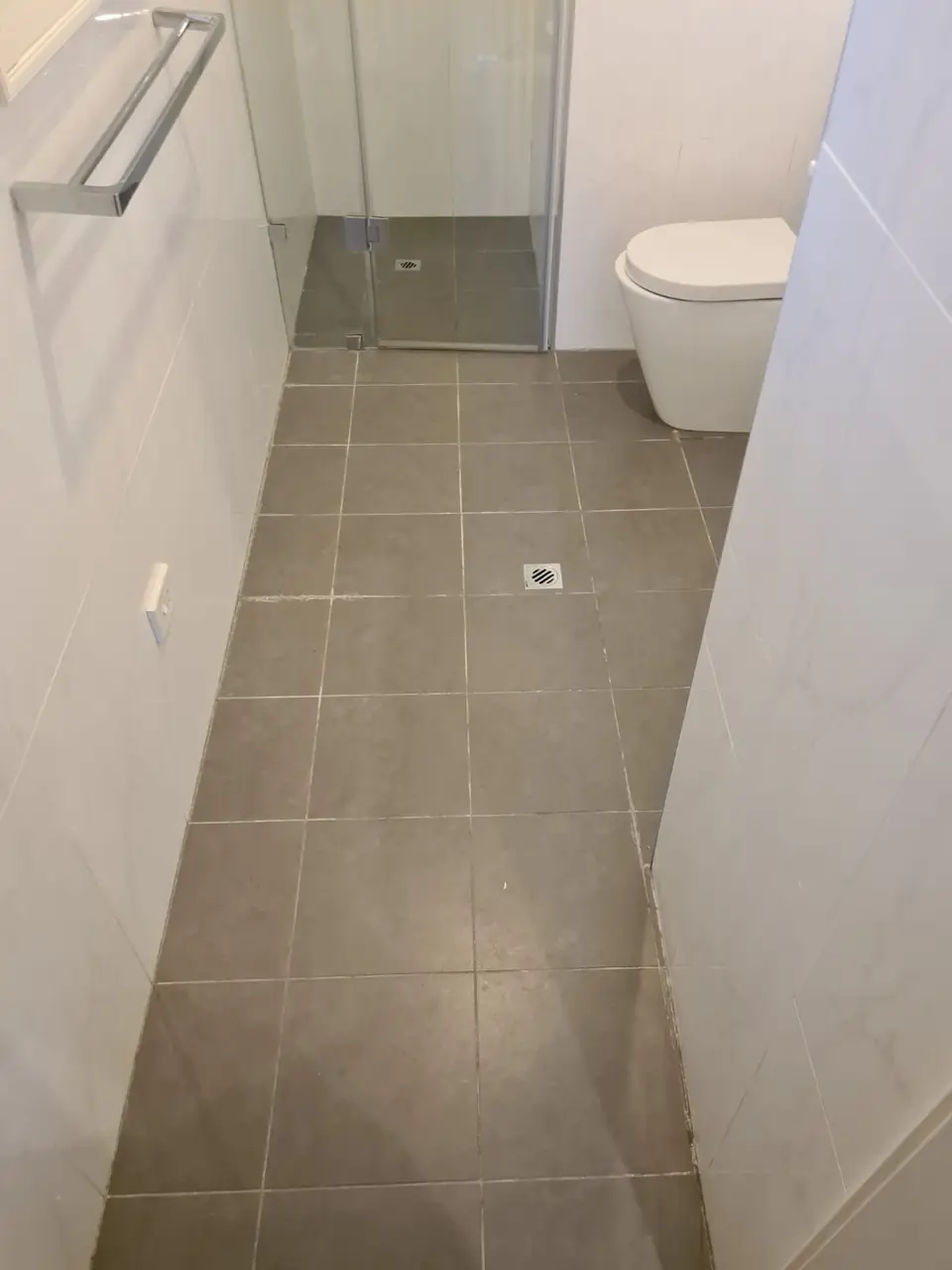 Before: Grey-tiled bathroom floor leading to a walk-in shower, with dull grout