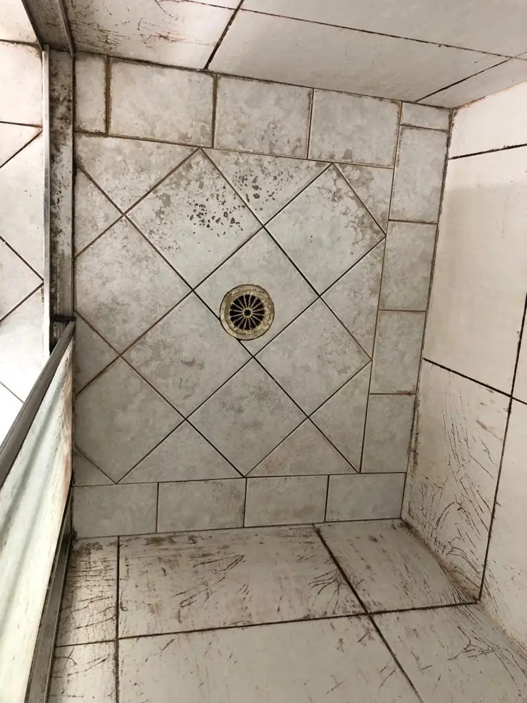 Before: Grey diagonal-pattern shower base with dark stained grout and joints