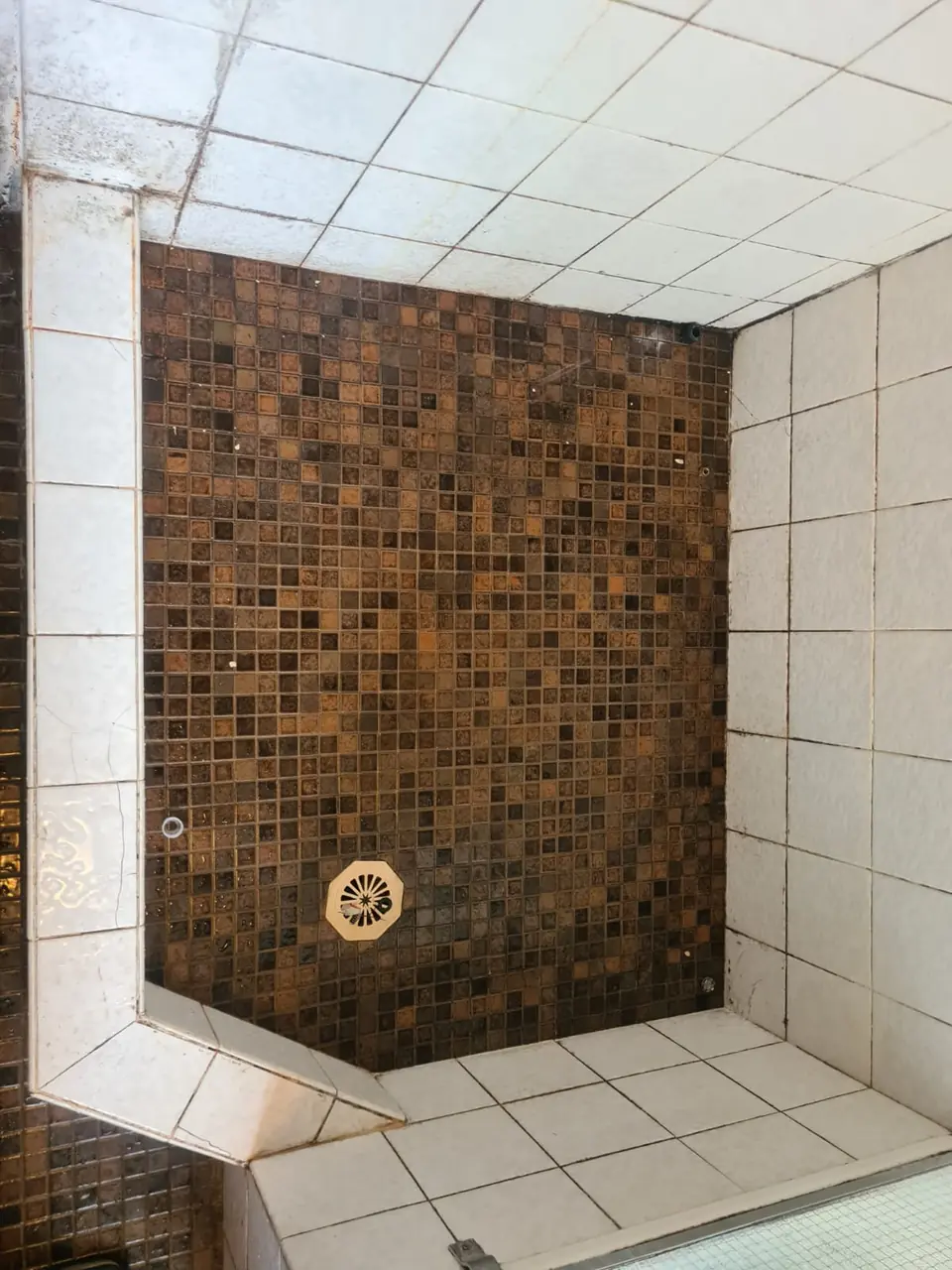 Before: Brown mosaic shower floor with a white-tiled hob, grout and edges stained