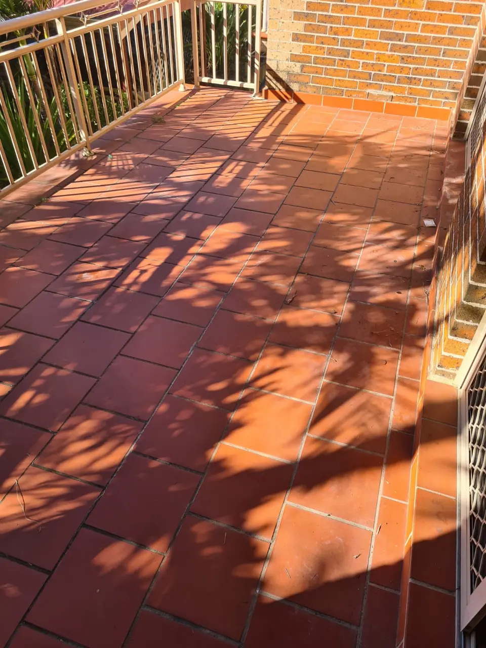 Before: Terracotta-tiled balcony with brick walls and a metal balustrade, tiles dull and grout weathered