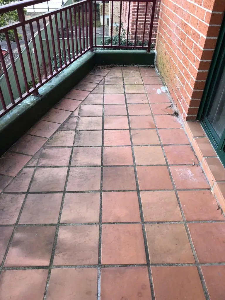 Before: Terracotta-tiled balcony with green upstands and dark, dirty grout lines