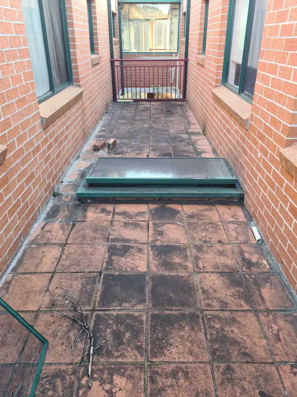 Before: Narrow tiled walkway between brick walls with heavy black staining across tiles and grout