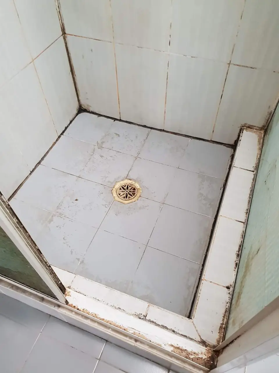 Before: White-tiled shower base with stained corners and deteriorated hob edges and sealant